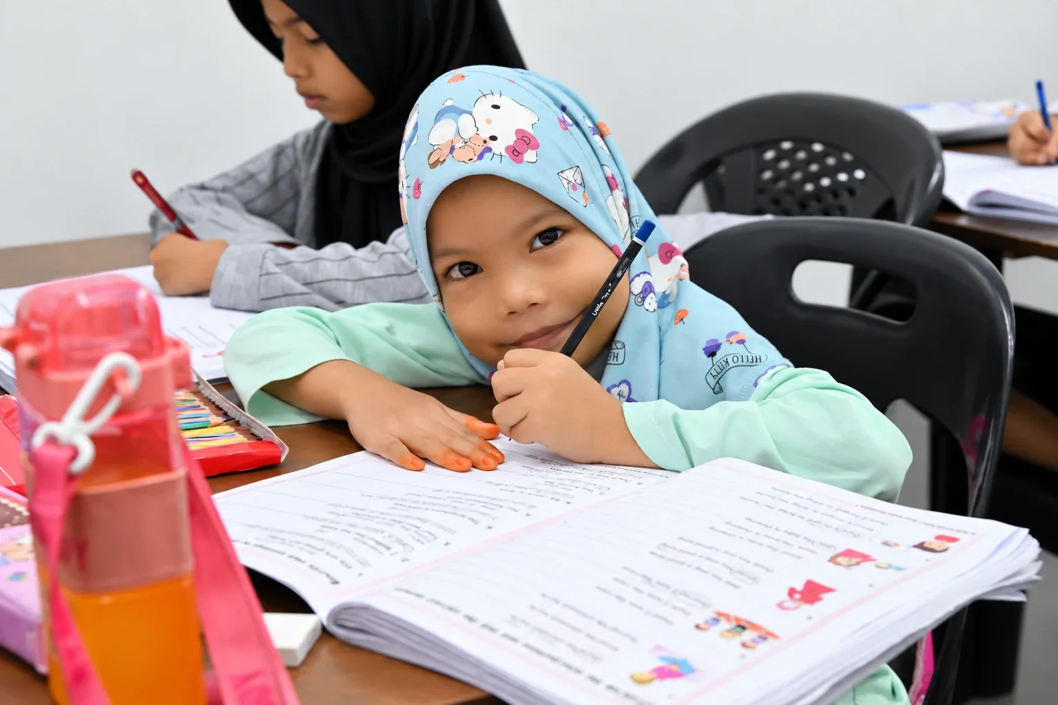 Pelajar Smart English bertudung biru muda bersama buku latihan Bahasa Inggeris