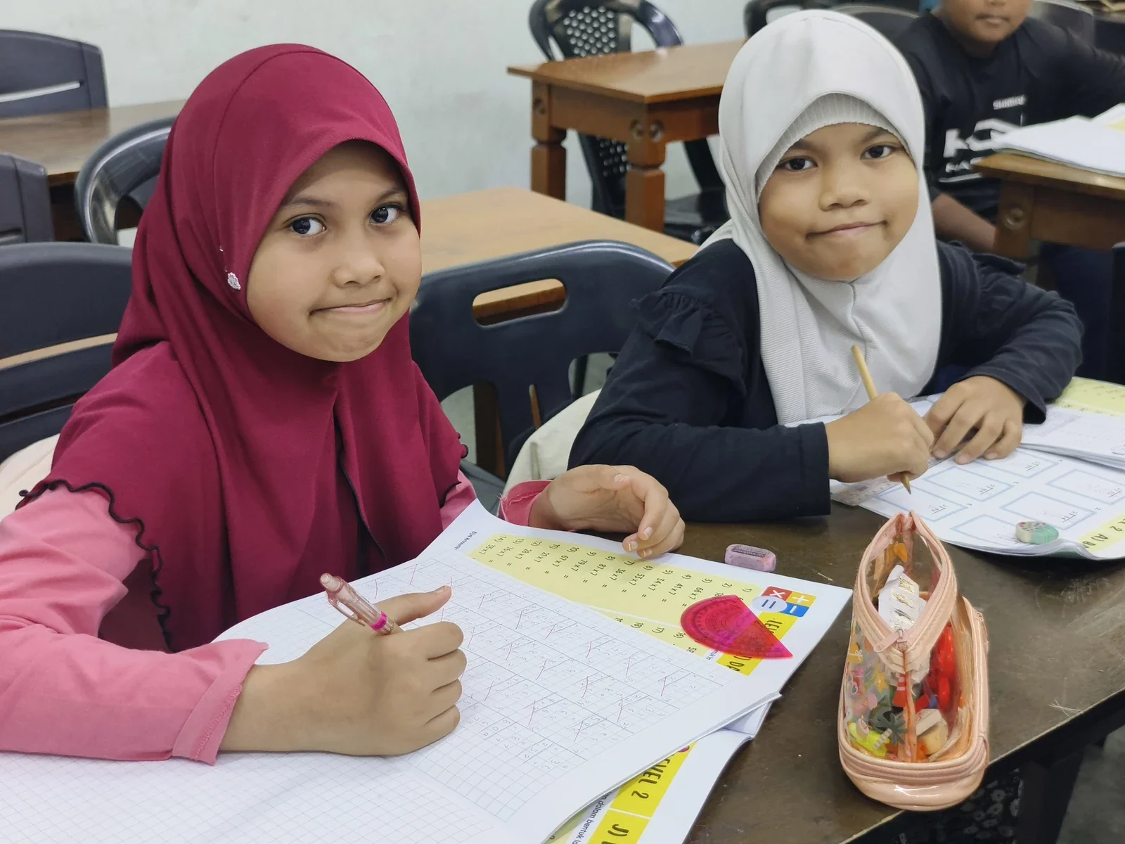 Pelajar kelas Intermediate bersama buku latihan Matematik.