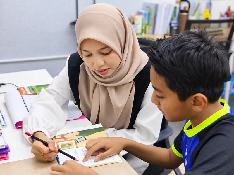 Guru ALC membimbing seorang pelajar membaca buku secara one-to-one.